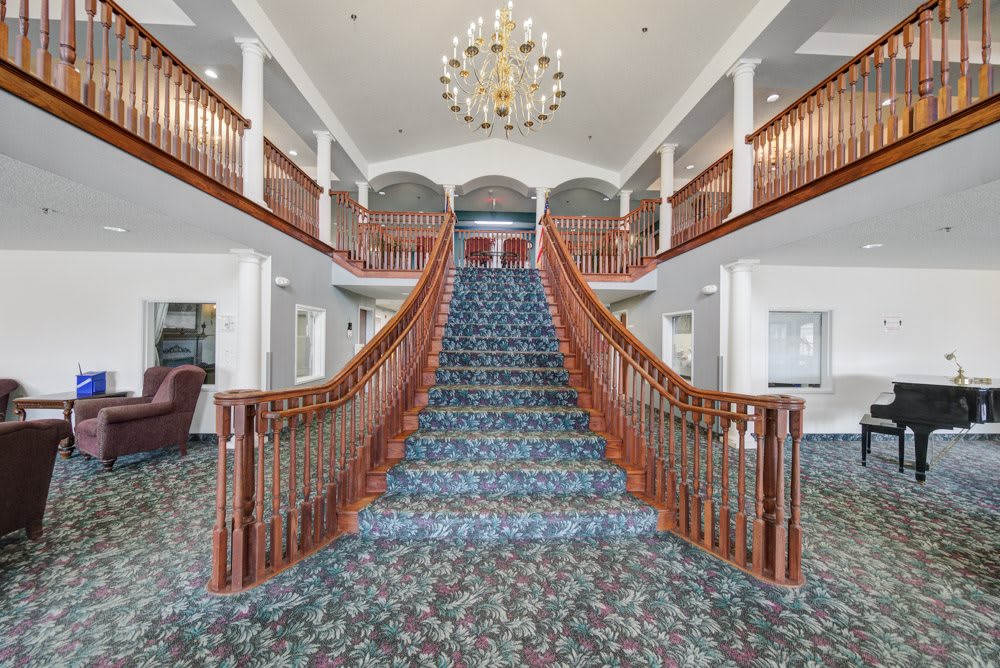 A grand, carpeted staircase with wooden railings and a large chandelier in an elegant interior setting.
