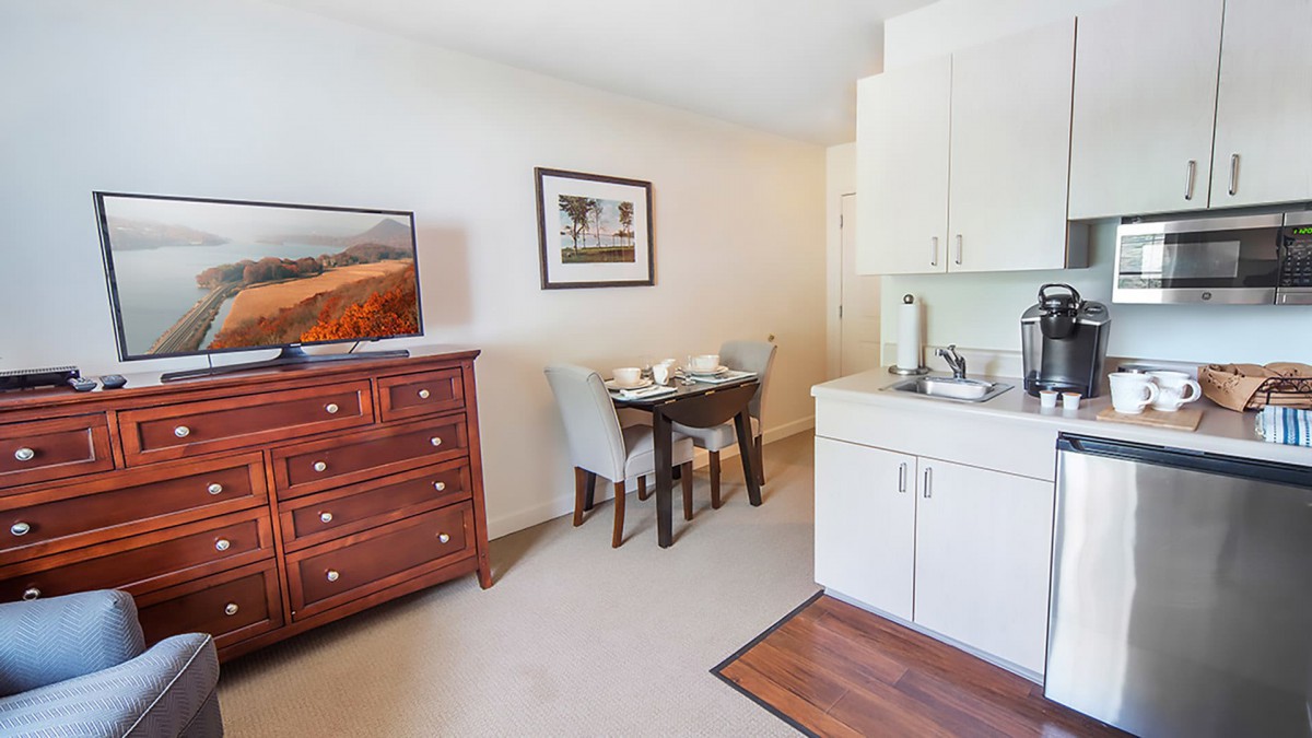 A cozy room featuring a television on a dresser, a small dining table with chairs, and a kitchenette area.