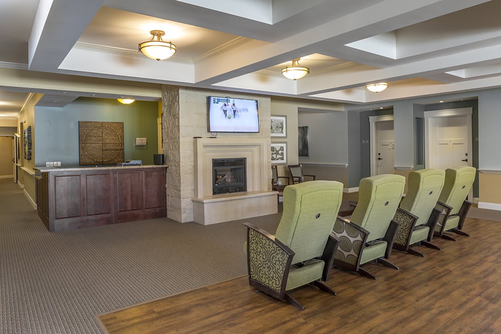 A comfortable lounge area with a row of chairs facing a fireplace and a television, adjacent to a reception desk.