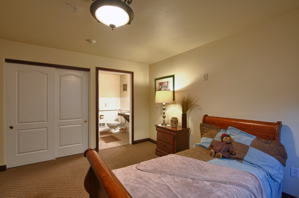 A cozy bedroom with a wooden bed, bedside lamp, and open door to a bathroom.