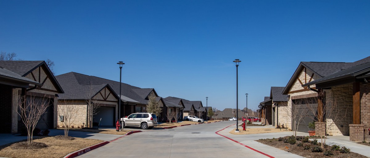 A quiet suburban street lined with houses and parked cars on a clear day.