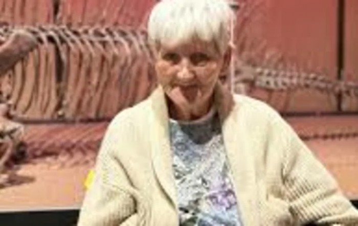 An elderly woman with white hair wearing a cardigan indoors.