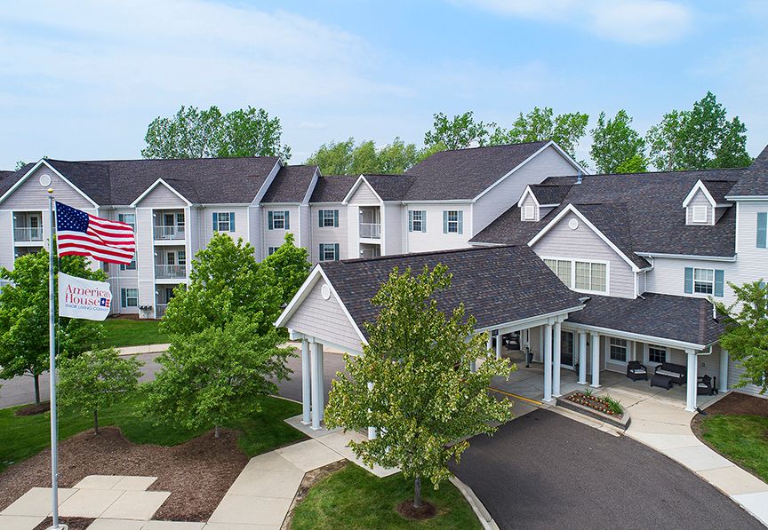 A residential building with a welcoming entryway, surrounded by trees and displaying a flag.