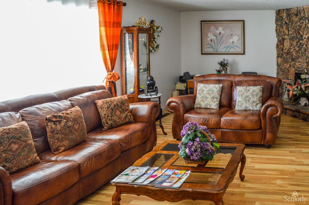A cozy living room featuring leather sofas, a wooden coffee table with a floral centerpiece, and elegant curtains.