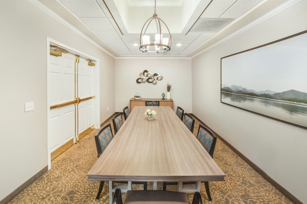 A modern meeting room with a long conference table, surrounded by chairs and decorated with wall art and contemporary lighting.