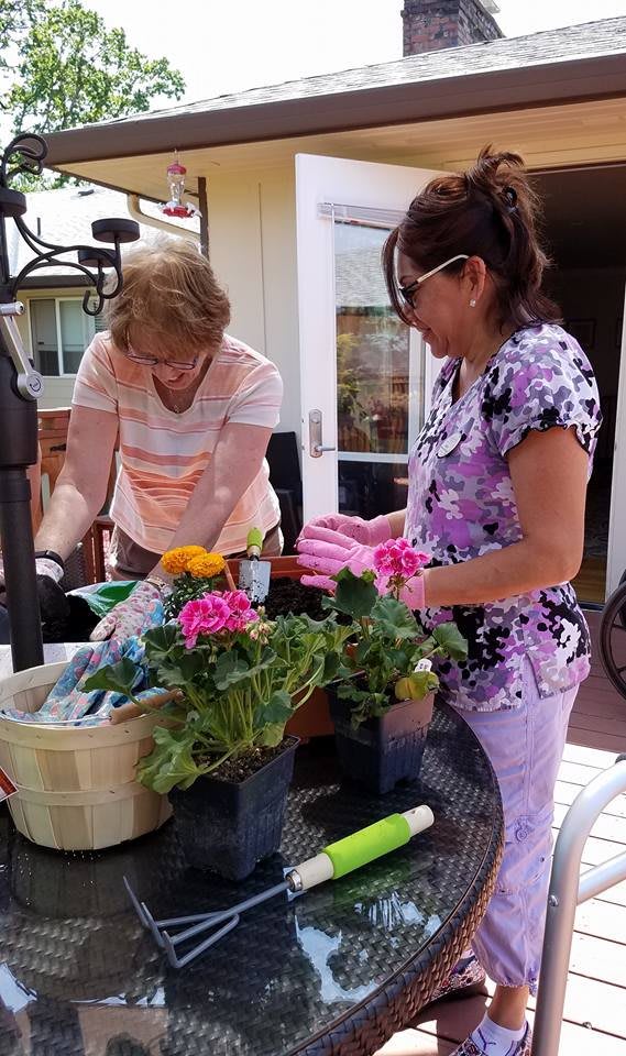 Two women engaged in gardening, arranging flowers in pots outdoors.