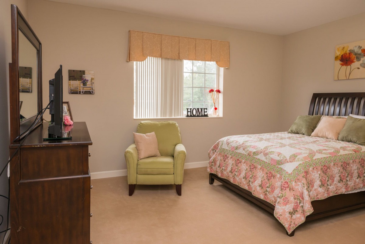 A cozy bedroom with a floral bedspread and a light green armchair by the window.