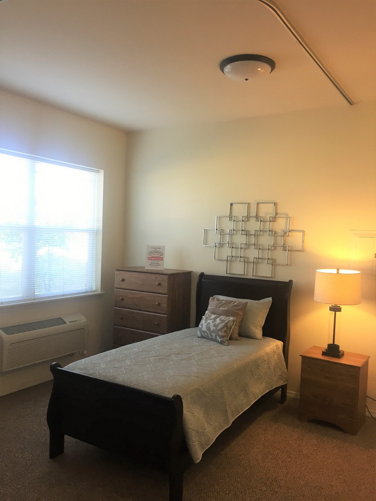 A cozy bedroom with a single bed, dresser, and lamp by the window.