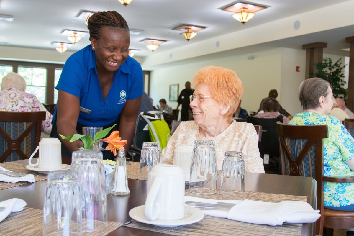 A staff member provides friendly service to a seated customer in a restaurant setting.