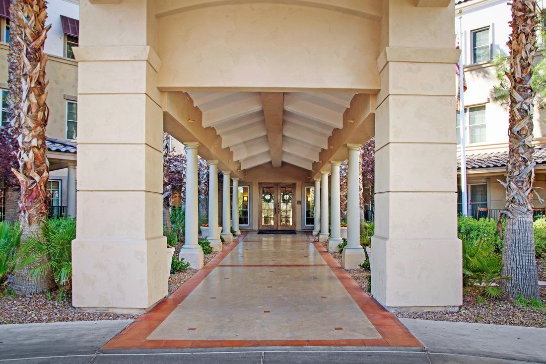 A symmetrical view of a covered walkway with columns and arches leading to a building entrance.