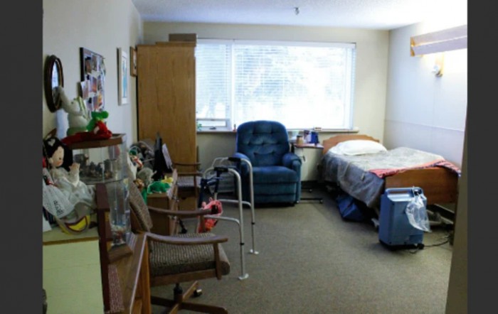 A cozy bedroom with a bed, chair, and walker by the window.