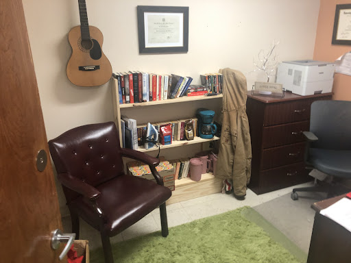 A cozy office space featuring a bookshelf filled with books, a comfortable chair, and a guitar on the wall.