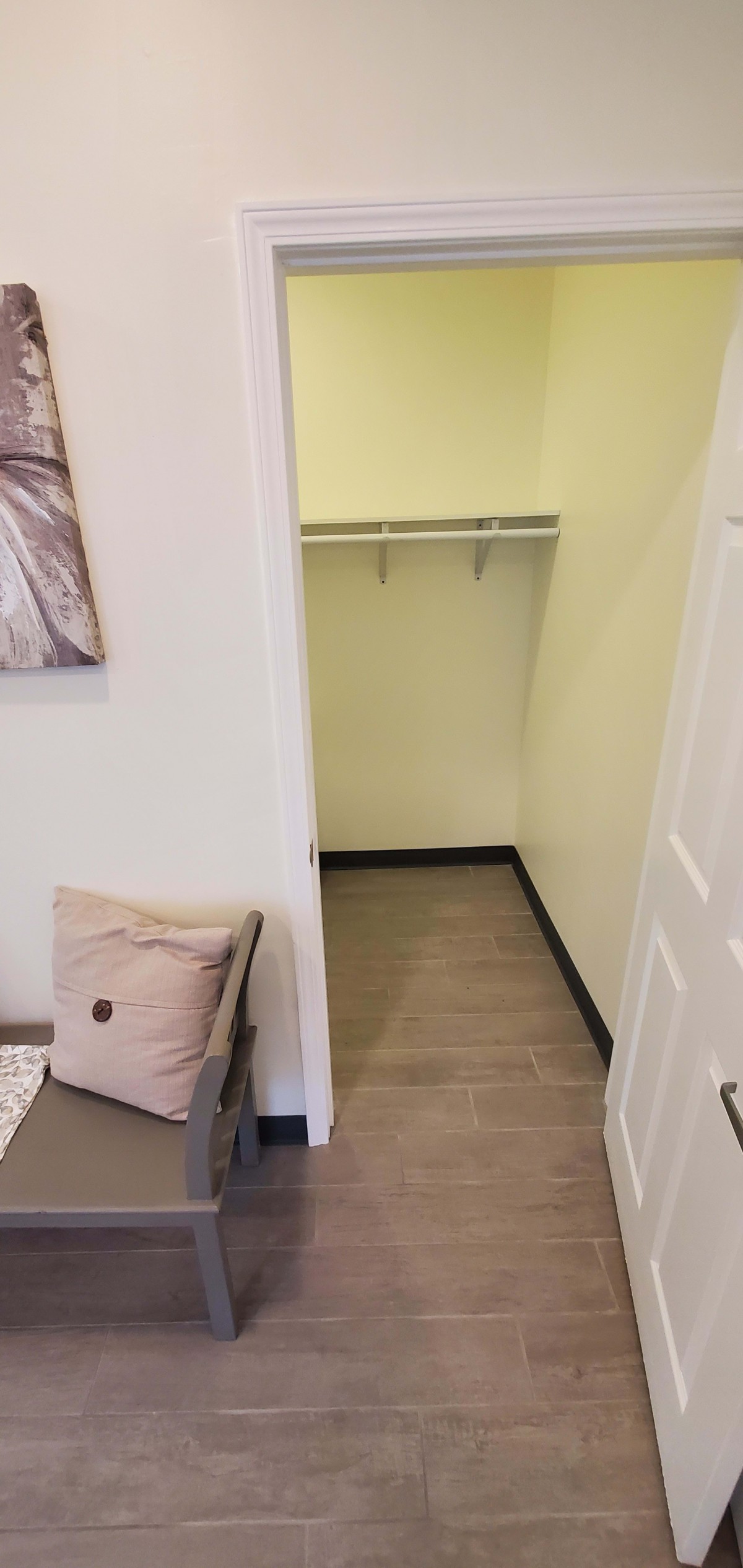 An empty walk-in closet with shelving and a bench with a pillow nearby.