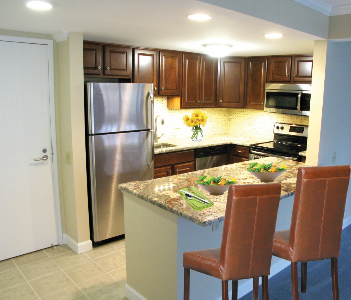 A modern kitchen with stainless steel appliances and granite countertops, featuring wooden cabinets and bar stools.