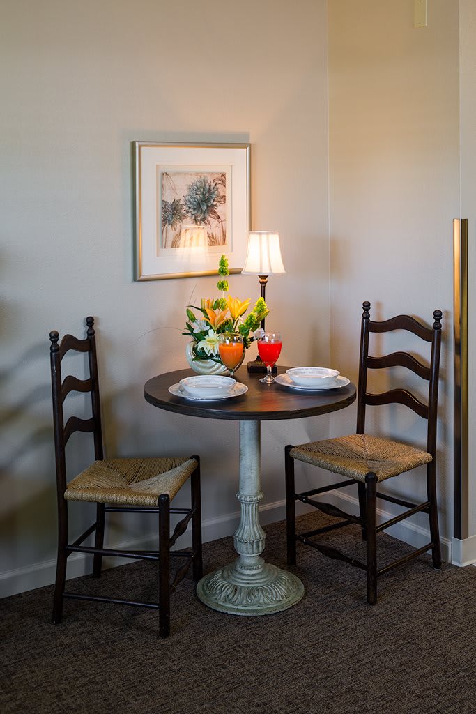 A cozy dining setup with a small round table and two chairs adorned with flowers and a lamp.