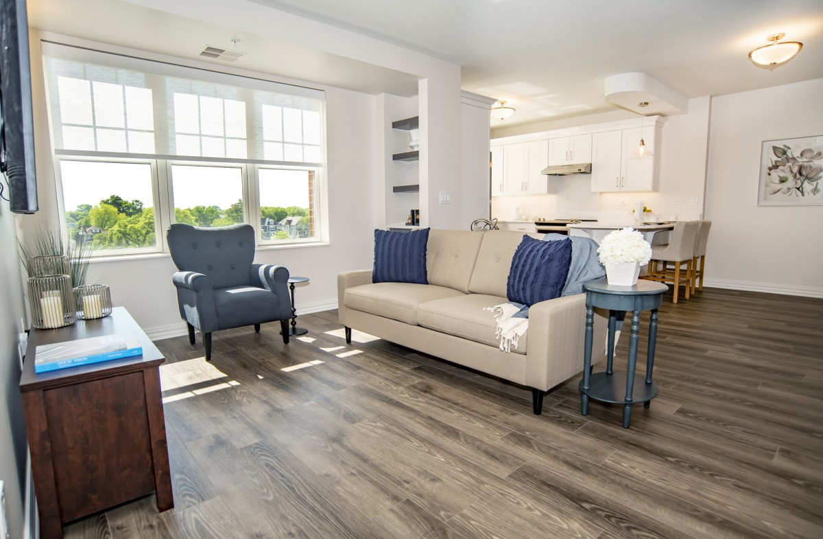 A modern, well-lit living room with a beige couch, armchair, and wooden flooring.