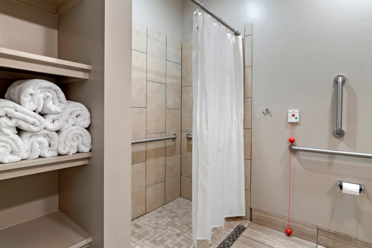 Modern bathroom with a tiled shower and neatly stacked towels on open shelving.