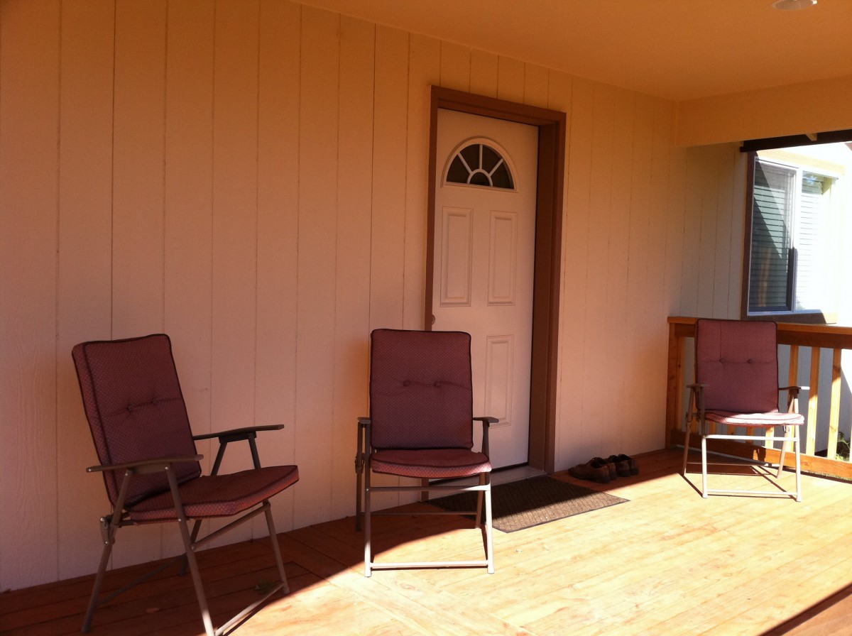 A sunny porch with three chairs and a door.