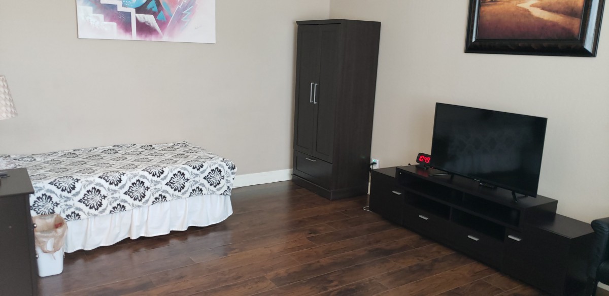 A minimalist bedroom with a small wardrobe, television, and wooden flooring.