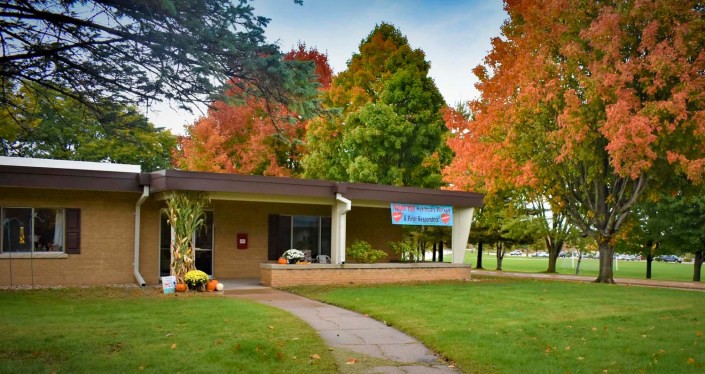 A small building surrounded by colorful autumn trees with a pathway leading to its entrance.