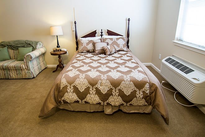 A cozy bedroom with a patterned comforter, wooden bedposts, and ambient lighting.