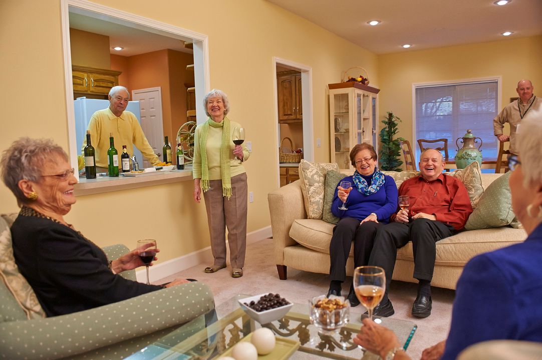 A group of seniors enjoying a social gathering in a cozy living room with drinks and conversation.