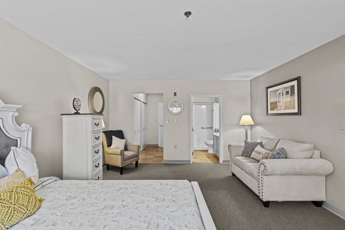 A cozy bedroom with neutral tones, featuring a comfortable armchair, a dresser, and elegant lighting.
