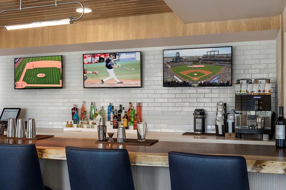 A bar area with three televisions displaying baseball games above a counter stocked with various drinks.