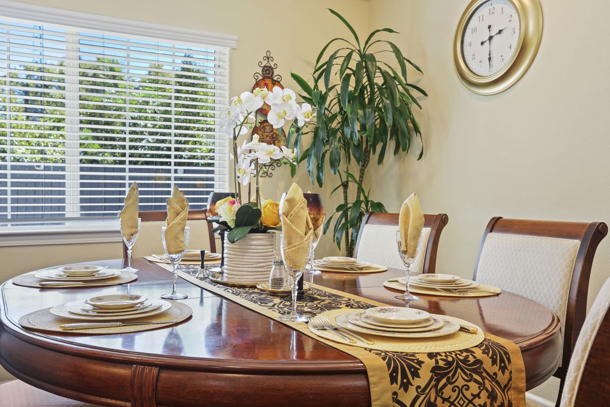 An elegantly set dining table with decorative dinnerware, a table runner, and a central plant arrangement.