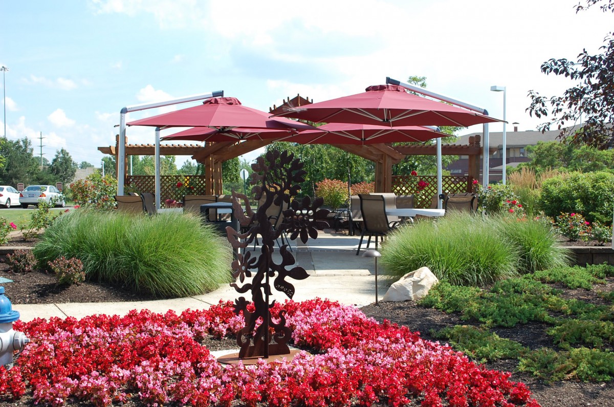 A beautifully landscaped garden with red flowers and large patio umbrellas providing shade over seating areas.
