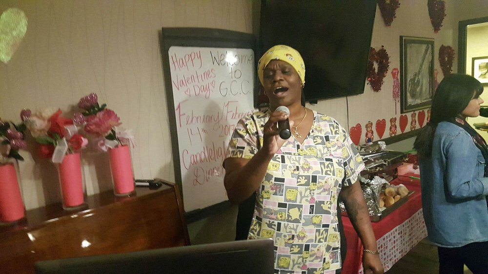 A person singing into a microphone indoors with a whiteboard in the background.
