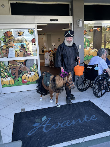 A man in a costume with a dog, celebrating the fall season outside a facility.