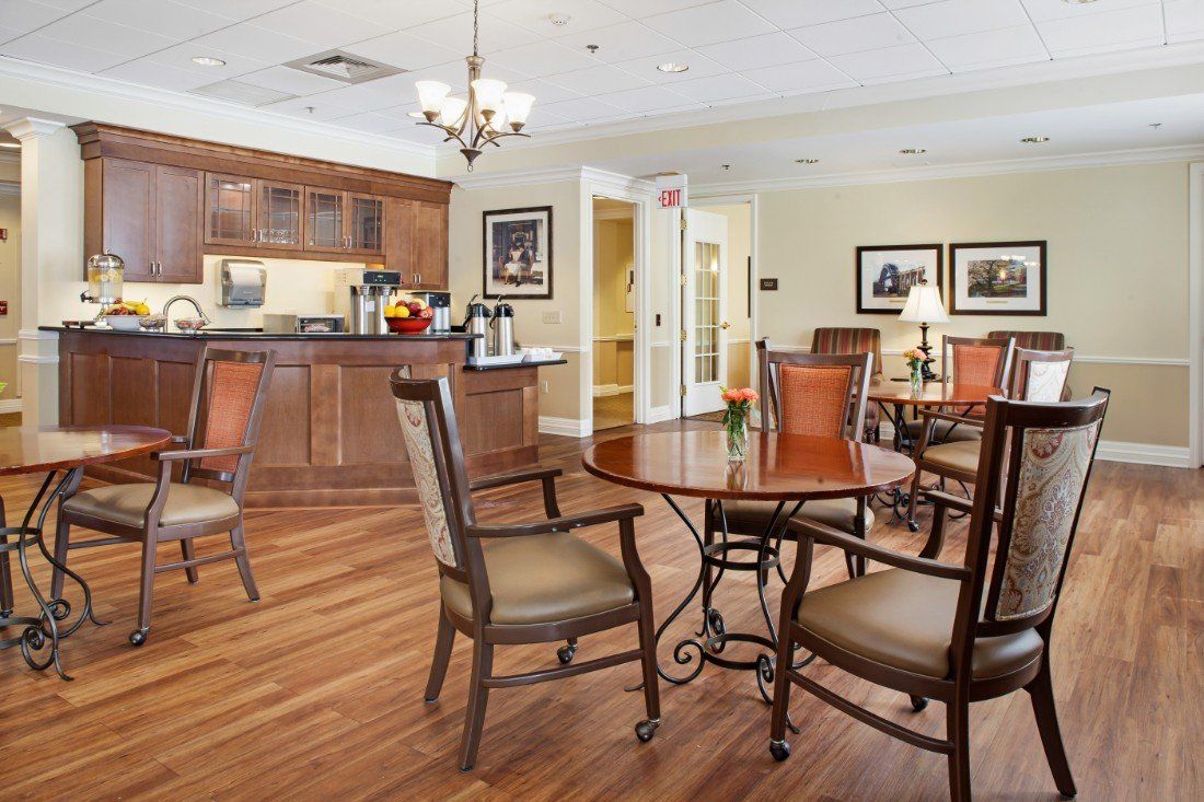 A cozy dining area with wooden flooring, featuring tables and chairs arranged near a kitchenette.