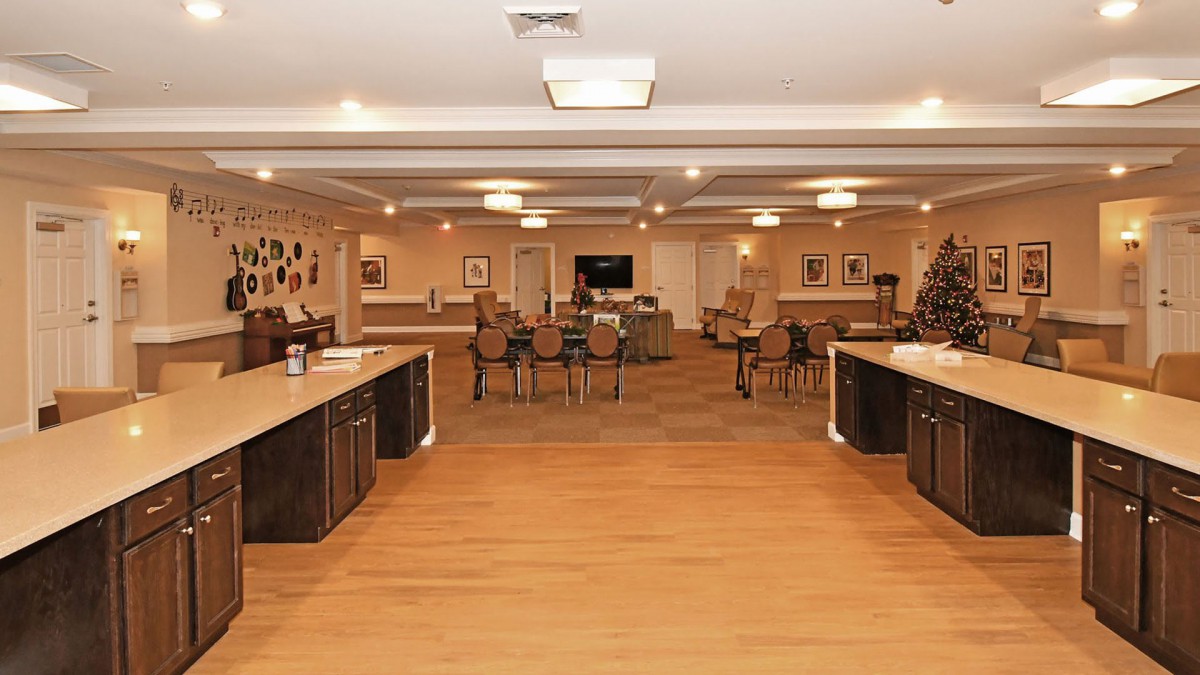 A spacious interior room with wooden flooring, multiple chairs and tables, and well-lit overhead lighting.