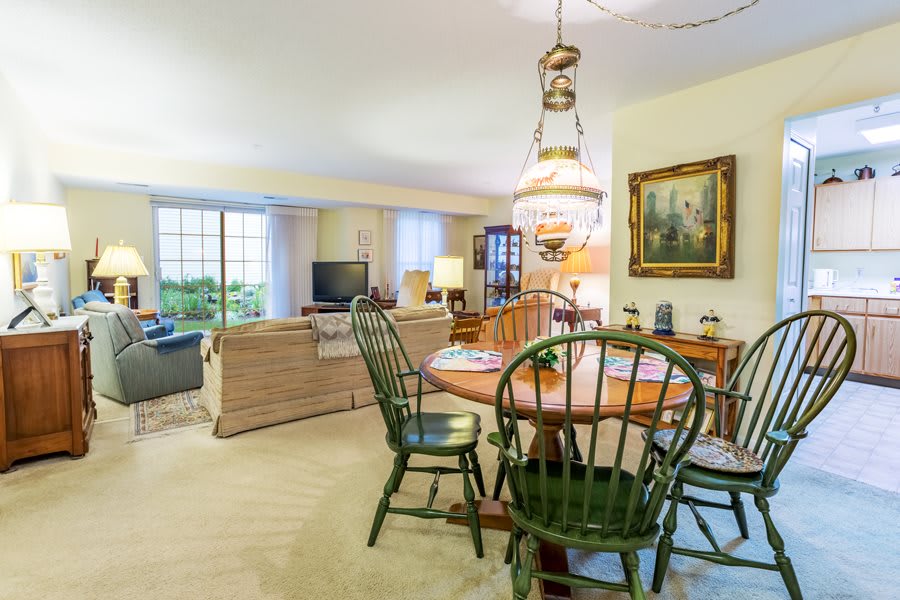 A cozy living and dining area featuring a round wooden table with chairs, a sofa, and decorative elements such as a lamp and painting.