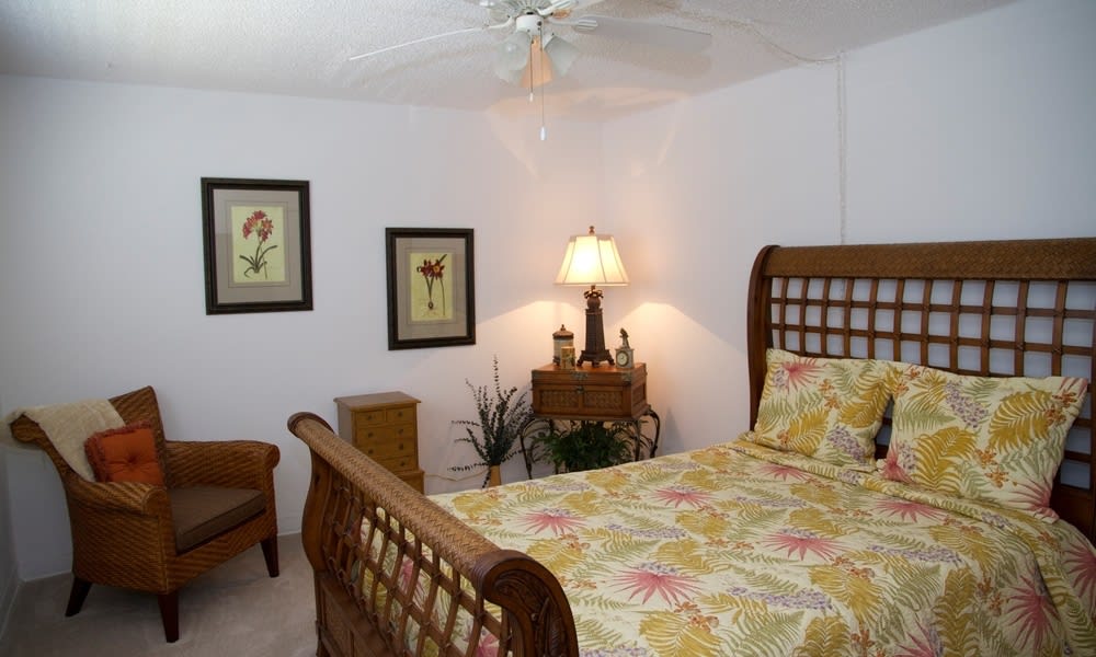 A cozy bedroom with a wooden sleigh bed, floral bedding, and warm lighting from a bedside lamp. The room is decorated with framed artwork and a touch of greenery.