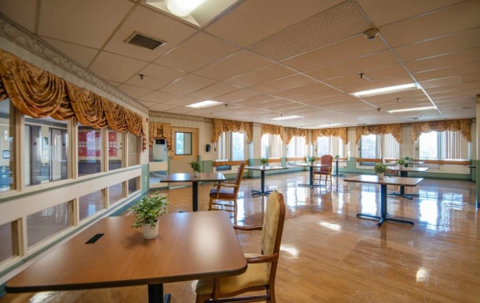 A spacious dining area with tables and chairs, surrounded by large windows that allow natural light to flood the room.