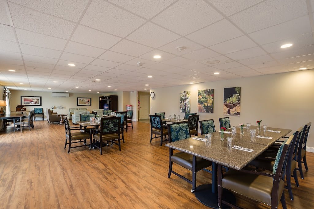 A spacious dining area with neatly arranged tables and chairs, featuring wooden flooring and ceiling lights.