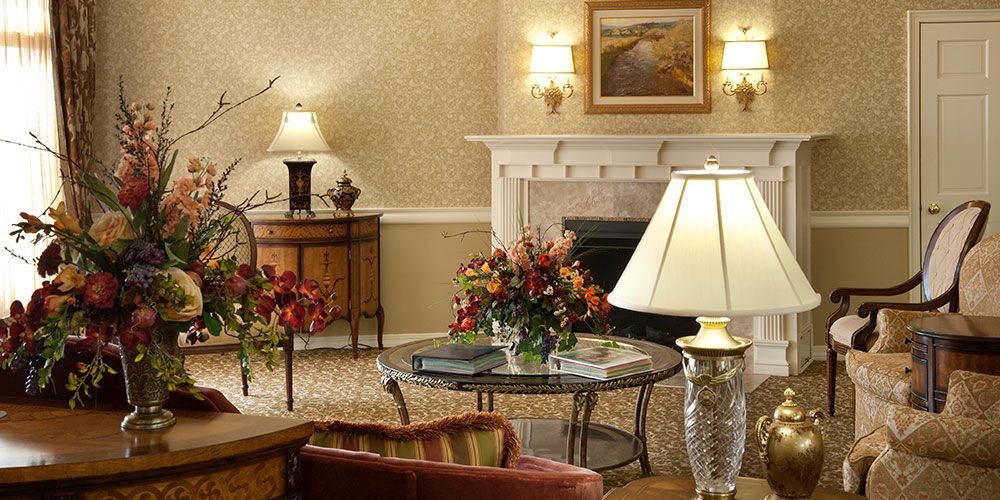 A cozy living room with elegant decoration, featuring a fireplace, lamps, and floral arrangements.