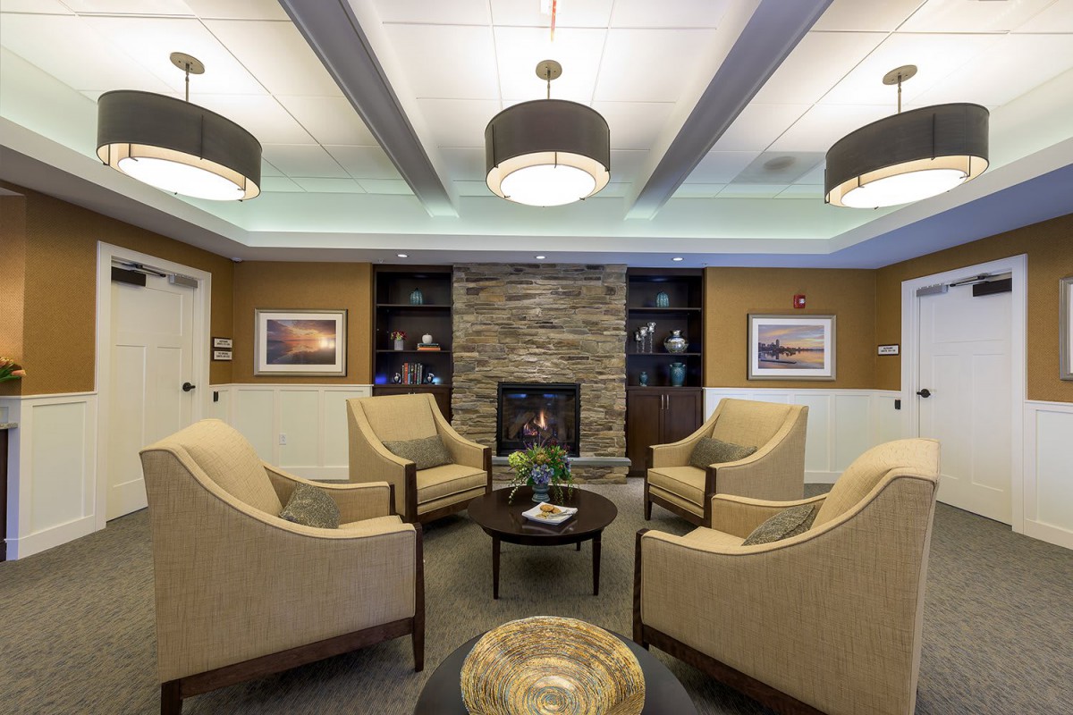 A cozy living room with armchairs arranged around a central fireplace, featuring modern decor and warm lighting.