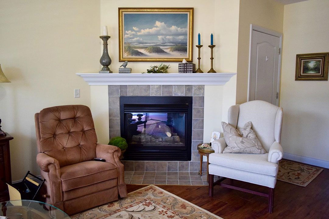 A cozy living room with a fireplace adorned with candles and painting, accompanied by a plush armchair and recliner.