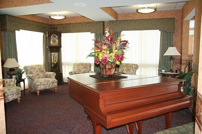 A cozy living room interior featuring a piano, flower arrangement, and a grandfather clock.