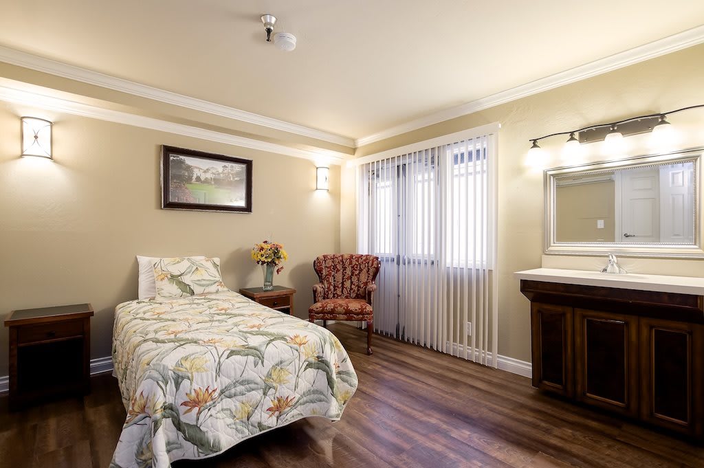 A cozy bedroom with a single bed, an armchair, and hardwood flooring.