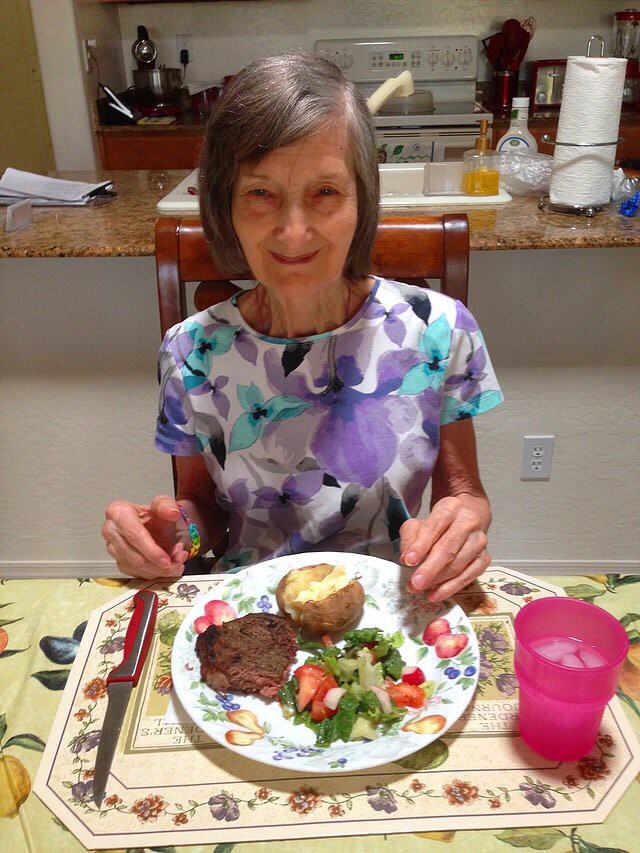 A woman sitting at a dining table enjoying a meal consisting of steak, salad, and a baked potato.