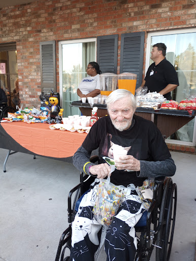 An elderly man enjoys a moment at an outdoor social gathering, surrounded by food and joyful company.
