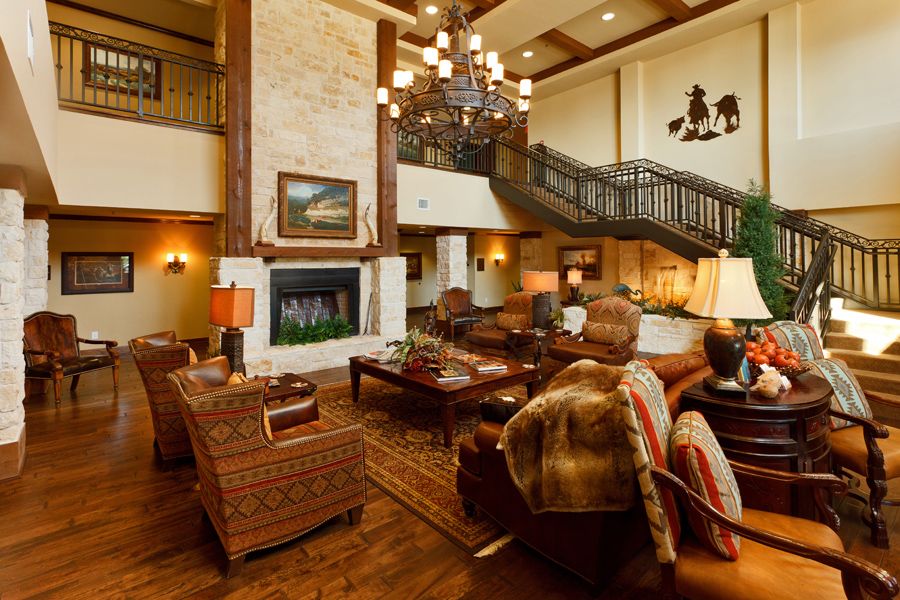 A spacious living room with warm lighting, featuring a large fireplace and elegant wooden furniture under a high ceiling.