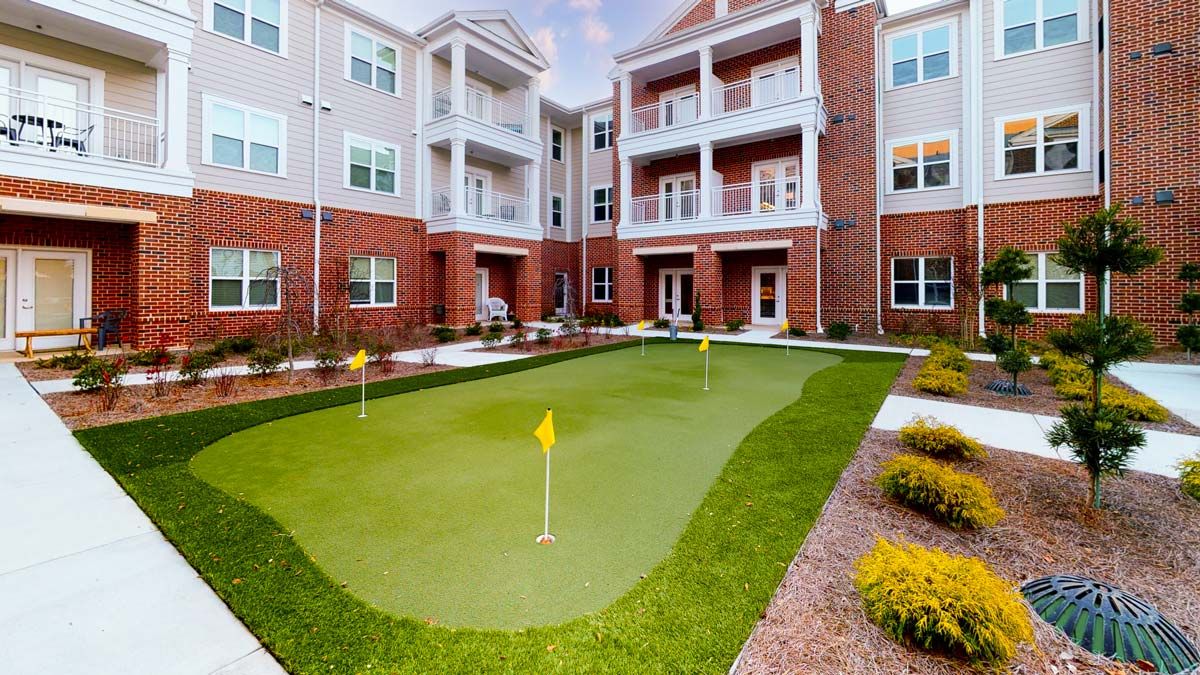 A modern apartment complex with a neatly maintained outdoor putting green surrounded by landscaping.