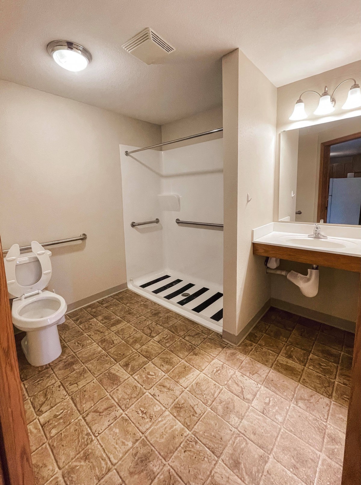 An accessible bathroom featuring a walk-in shower, toilet, sink, and safety grab bars.