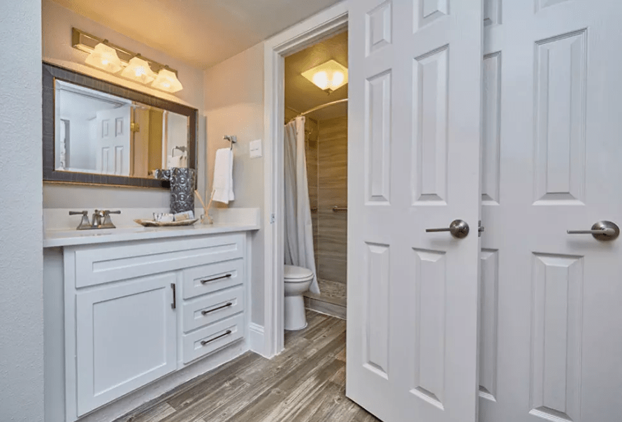 A modern bathroom with a vanity, sink, and a mirror adjacent to a shower area.
