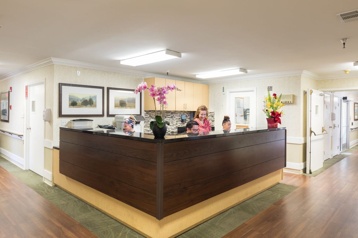 A welcoming office reception area with a wooden desk, decorative flowers, and framed art on the walls.